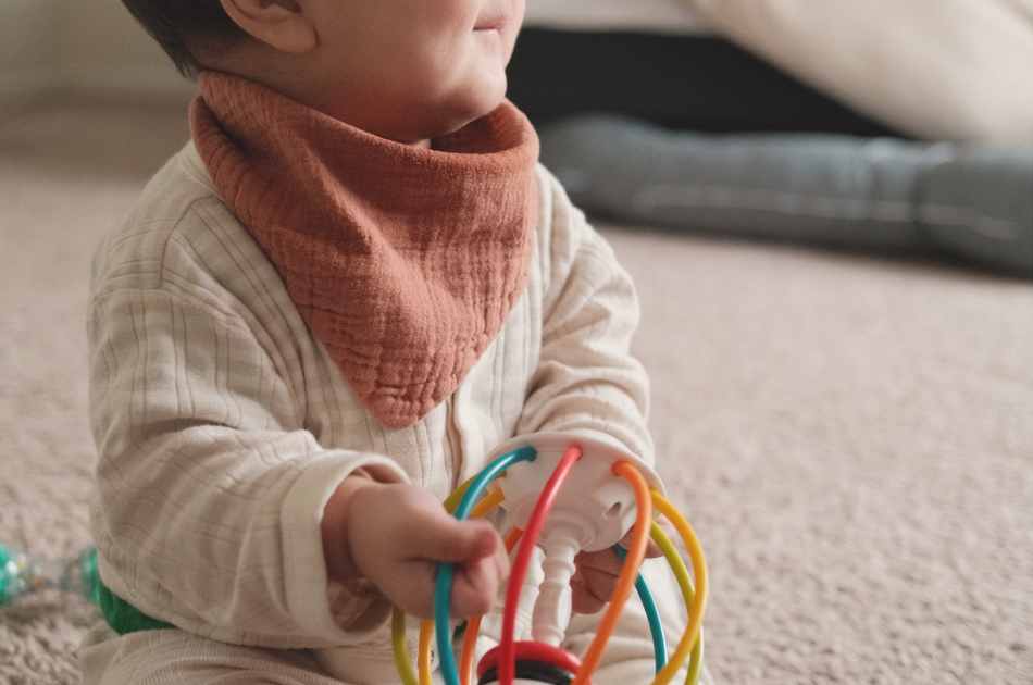 Seven-month-old baby sitting independently and playing with a colorful toy on the living room floor