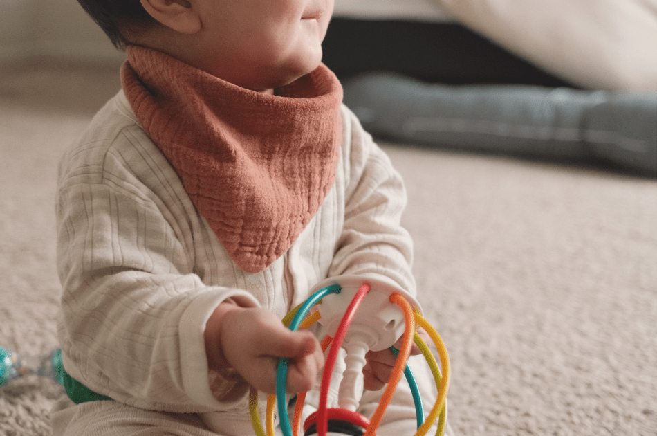 Seven-month-old baby sitting independently and playing with a colorful toy on the living room floor